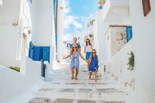 Familie mit zwei Kindern in weiß blauen Klamotten läuft eine weiße Gasse in einem griechischem Ort hinunter