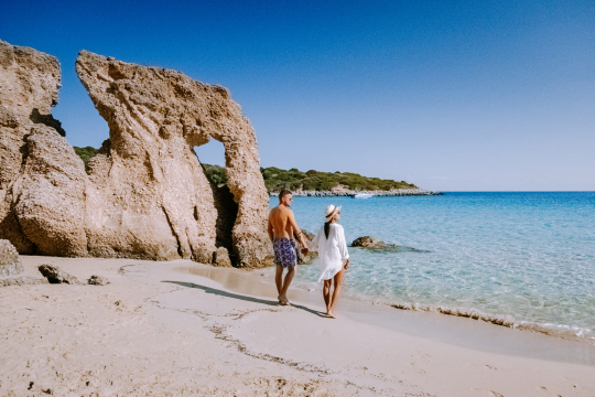 Paar am Strand auf Kreta, im Hintergrund einige Felsen und hellblaues Meer rechts